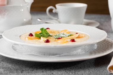 Beyaz kasede dilimlenmiş muzlu Semolina lapası ya da kahvaltı yulafı gri taş arka planda izole edilmiş. Ev yapımı yemek. Lezzetli bir kahvaltı. Seçici odaklanma. Yatay fotoğraf. Bardak ve çaydanlık..