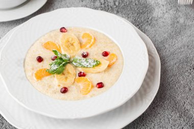 Beyaz kasede dilimlenmiş muzlu Semolina lapası ya da kahvaltı yulafı gri taş arka planda izole edilmiş. Ev yapımı yemek. Lezzetli bir kahvaltı. Seçici odaklanma. Yatay fotoğraf. Bardak ve çaydanlık..