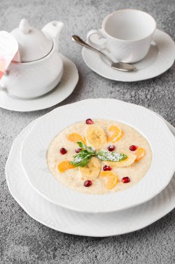 Beyaz kasede dilimlenmiş muzlu Semolina lapası ya da kahvaltı yulafı gri taş arka planda izole edilmiş. Ev yapımı yemek. Lezzetli bir kahvaltı. Seçici odaklanma. Dikey fotoğraf. Bardak ve çaydanlık..