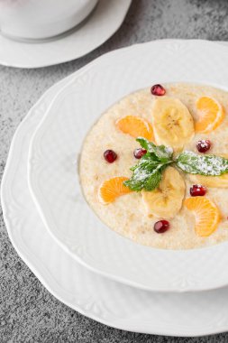 Beyaz kasede dilimlenmiş muzlu Semolina lapası ya da kahvaltı yulafı gri taş arka planda izole edilmiş. Ev yapımı yemek. Lezzetli bir kahvaltı. Seçici odaklanma. Dikey fotoğraf. Bardak ve çaydanlık..