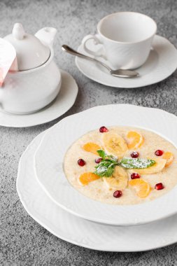 Beyaz kasede dilimlenmiş muzlu Semolina lapası ya da kahvaltı yulafı gri taş arka planda izole edilmiş. Ev yapımı yemek. Lezzetli bir kahvaltı. Seçici odaklanma. Dikey fotoğraf. Bardak ve çaydanlık..