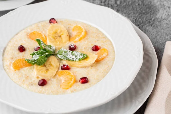 Gachas de sémola o avena de desayuno con plátanos en rodajas en tazón blanco aislado sobre fondo de piedra gris. Comida casera. Sabroso desayuno. Enfoque selectivo. Foto horizontal. Taza y tetera . — Foto de Stock