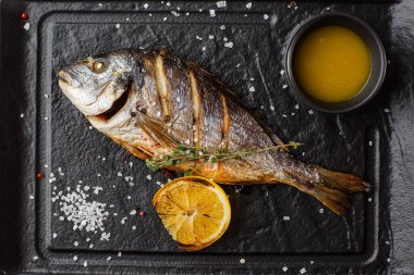 Lezzetli ızgara dorado ya da limon dilimleri, baharatlar, koyu taşlı biberiye. Izgara deniz balığı, zeytinyağı, baharat ve limon yenmeye hazır. Dorado, bitkiler ve baharatlar. Menü fotoğrafı