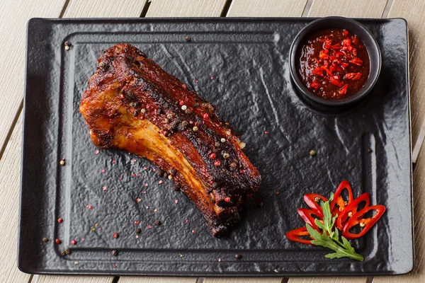 stock image Grilled and barbecue hot pork ribs with hot chilli pepper and hot sauce on black stone background. Isolated. Dish for men. Spicy