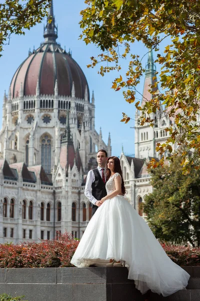 Panna młoda i pan młody przytulają się na ulicy starego miasta. Ślub para spacery w Budapeszcie w pobliżu Parliament House. Biała, szczęśliwa, romantyczna para świętująca swoje małżeństwo. Koncepcja wesela i miłości. — Zdjęcie stockowe