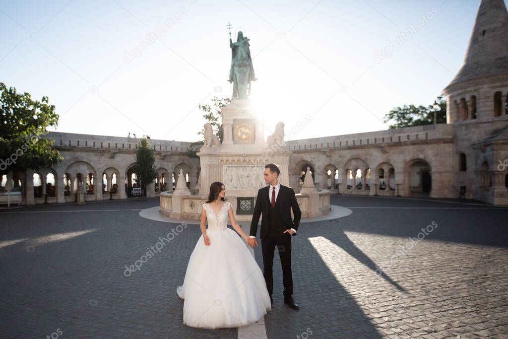 Bride and groom hugging in the old town street. Wedding couple walking on the Fishermans Bastion, Budapest, Hungary. Happy romantic young couple celebrating their marriage. Wedding and love concept.