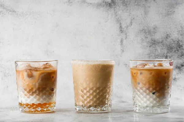 Three glasses with cold brew coffee and milk and ice cocoa isolated on bright marble background. Overhead view, copy space. Advertising for cafe menu. Coffee shop menu. Horizontal photo.