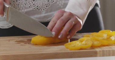 Modern bir mutfağın ahşap tahtasında sarı dolma biber kesen kadın ellerine yakın çekim. Sağlıklı beslenme. - Evet. Kız sebzeleri salata kasesine koyuyor. Salata hazırla. 6K Blackmagic kamerasıyla çekildi..