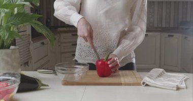 Kadın ellerine yakın çekim modern bir mutfakta ahşap tahtada kırmızı dolma biberin üst ve çekirdeğini kaldırır. - Evet. Kız sebzeleri salata kasesine koyuyor. Salata hazırla. 6K Blackmagic kamerasıyla çekildi..