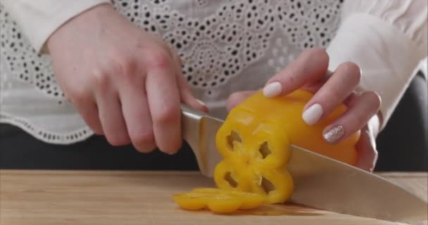 現代的なキッチンで木製ボード上の黄色の鐘唐辛子を切断女性の手の閉鎖。健康的な食事。そうだ。少女は野菜をサラダボウルに入れます。サラダを用意する。6kで撮影｜Blackmagic Camera. — ストック動画