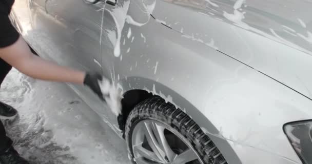 Чоловіча рука з пінною губкою, що миється на срібному автомобілі. Концепція автосервісу, автомийка. Розповсюдження піни на блискучому екстер'єрі автомобіля повільний рух. Автомийка або деталізовані ціни. 4k — стокове відео