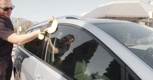 Een man veegt een carrosserie af nadat een auto gewassen is met een doek, droogt, verwijdert waterresten. Wasauto in een zelfbedieningscarwash. Auto detaillering - de man houdt de microvezel in de hand en polijst de auto. — Stockvideo