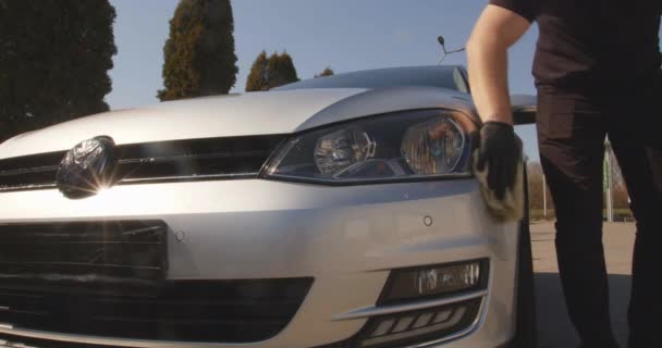 Um homem limpa um corpo de carro depois de uma lavagem de carro com um pano, seca, remove resíduos de água. Lavagem de carro em uma lavagem de carro self-service. Detalhes do carro - o homem segura a microfibra na mão e polir o carro . — Vídeo de Stock