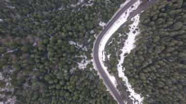 Karlı ormanda kış yolu üzerinde araba sürüyor, 4K 'daki insansız hava aracından hava görüntüsü. Uzun çam ağaçlarıyla kaplı ormanın hava manzarası güneşli bir günde uzun yollar boyunca taze karla kaplıydı..