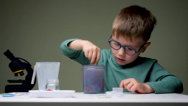 Το αγόρι με τα γυαλιά κάνει πειράματα. Νεαρός επιστήμονας μπερδεύει τις λίρες για πειράματα. Παίζουν σε κλειστό χώρο. Αρχική εργαστηριακή βάση — Αρχείο Βίντεο