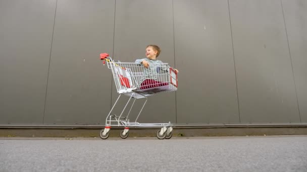 Concepto de compras. Una familia de padres. Padre con hermanos yendo al supermercado, al centro comercial. Feliz papá empujando el carrito de compras con niños alegres en él. Consumismo de la vida moderna. Fondo Brexit — Vídeo de stock