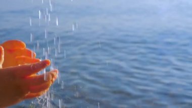 Çocuk elleri suyun damlalarına uzanıyor. Deniz manzarası arka planında küçük çocukların ellerinden akan su. Küçük çocuk elleri su damlalarına uzanıyor. Vücut parçası