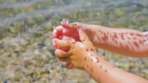 Drinking water drops falling on childs hands. Little hands playing with drops of water. Light and shadow from water drops on little kids hands. Sea background — ストック動画