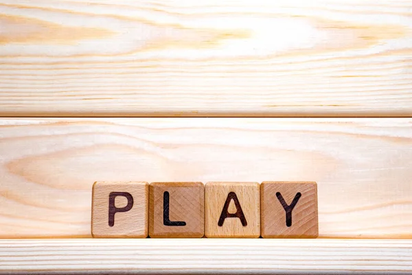 Wooden cubes form the word play. Word play formed with wooden cubes. Toy cubes made of wood on wooden background. Concept of play. Play sign background. Word formation
