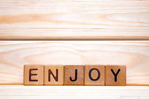 Word enjoy written on wooden cubes on wooden background. Wooden cubes formed the word enjoy. Entertainment concept. For wood latin letters made the word enjoy