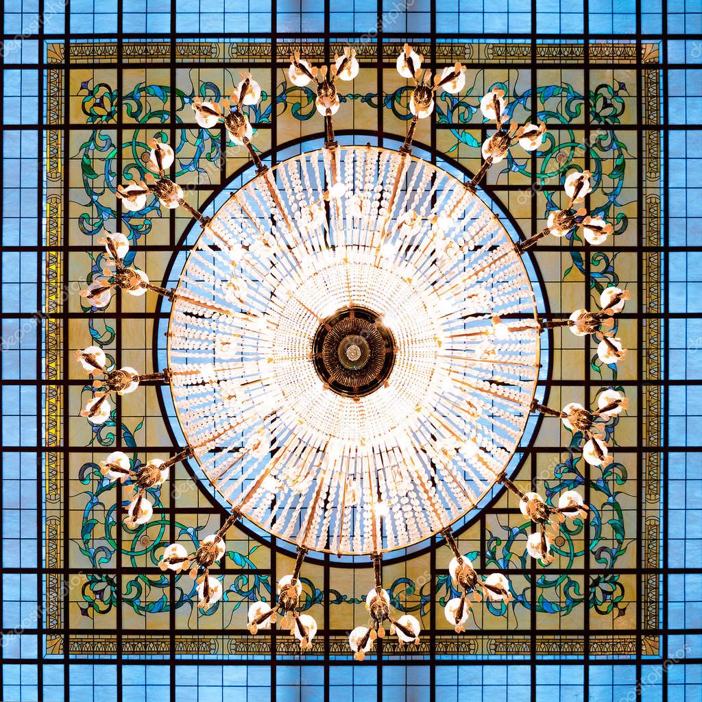Background of large chandelier hanging on the ceiling. Venetian glass background. Luxury background. Lights on the chandelier in restaurant, hotel, resort. Symmetric pattern. Square