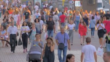 Şehirde yürüyen bir sürü insan. Şehir halkı işlek bir caddeye çıkıyor. Öğrenciler, turistler cadde boyunca gidiyor. Şehir manzarası. Bir grup insan, güneş gözlüklü turistler. Kalabalık.