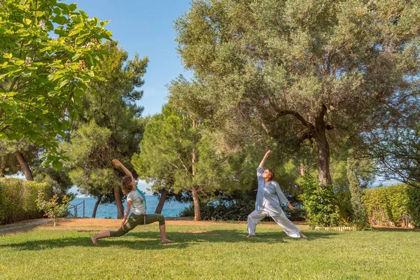 Two women doing yoga warrior pose. Healthy lifestyle. Strong body concept. Happiness concept. Happy mother with daughter spend time outdoor. Body care background. Strong muscles, flexibility of body