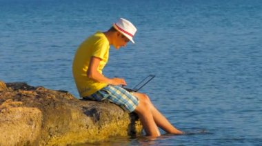 Genç hipster dizüstü bilgisayar kullanarak, turist kavramı. Tropik egzotik okyanusta dizüstü bilgisayarda çalışan adam. İnternet bağlantısı 3g, 4g. Sanal ofis. Seyahat ve iş. Erkek deniz kıyısında çalışır