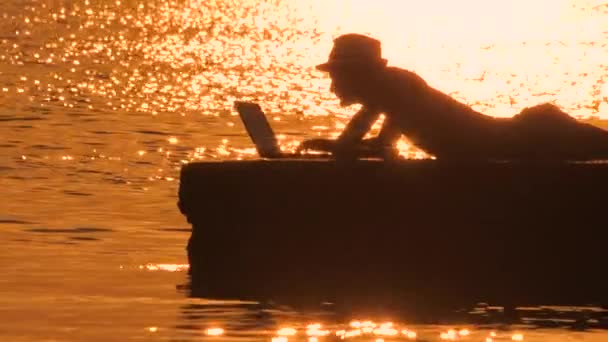 Šťastný muž ležící na kameni a pracující v počítači s výhledem na moře, statický rám, uprostřed pohledu. Muž s moderním laptopem sedí na pláži. vzdálená práce. Muž s laptopem u moře. Budoucí práce. — Stock video