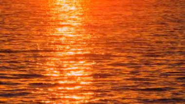 Gün batımının deniz suyuna yansıdığı manzaralı deniz manzarası. Yoldan geçen, elinde not defteri olan biri. Sıcak magma renk paleti. Gün batımında alışılmadık deniz manzarası. Deniz suyu günbatımını yansıtır. Deniz suyundaki yansıyan güneş.