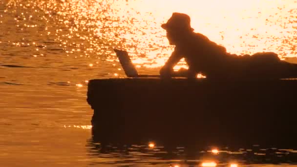 Hipster med anteckningsbok på havet solnedgång teckensnitt. Programmerare som skriver kod på den pittoreska stranden. En framgångsrik resebloggare som jobbar vid havet. Vacker solnedgång på havet. Framtida affärsidé — Stockvideo