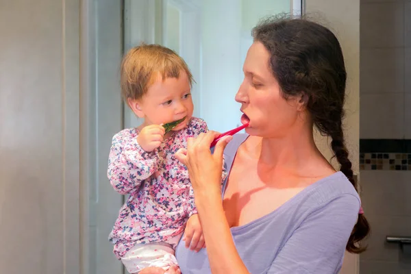 Малюк на руках матері чистить зуби матір'ю. Мати і дочка чистять зуби у ванній кімнаті. Перші зуби. Концепція стоматології. Мати з дитиною чистить зуби . — стокове фото