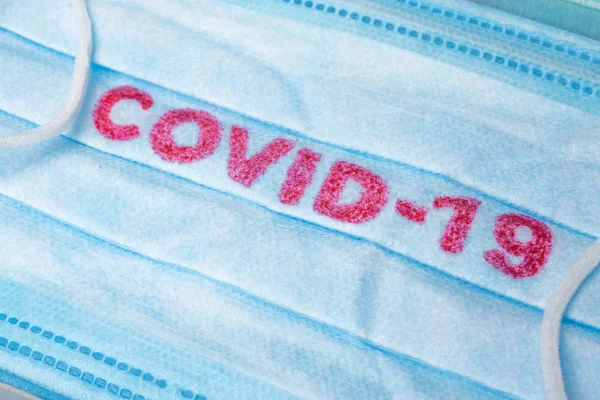 Blue Medical Disposable Face Mask with covid-19 printed on it. Covid-19 - Wuhan Novel Coronavirus pneumonia gets official name from WHO: COVID-19. Disposable breath filter face mask with earloop — Stock Photo, Image