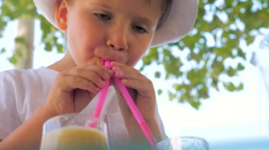 Little tourist drinking fresh juice outdoor. Refreshing drink with ice. Summer Cold drinks for hot summer. Young tourist drinks from two straws. Hipster in hat drinking fresh juice. Traveling concept