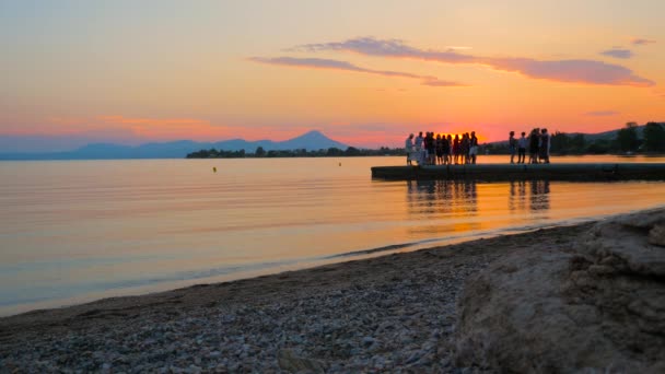 Sunset beach party. Sunset background with youth on the pier. Beach party on sunset. Outing party on the seaside. Holidays, event on the beach. Group of young people getting-together — Stockvideo