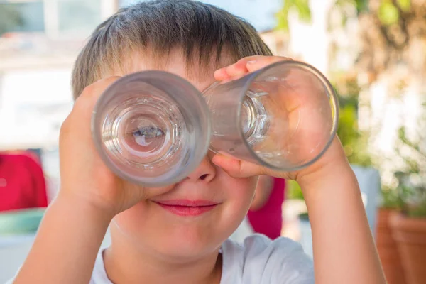 Boy looking through two glasses. Smiling boy. Funny kid joking. Summer vacation. Waiting for order at cafe, cafeteria, tavern. Child entertaining himself outdoor. Waiting for parent. Travel binoculars — 图库照片