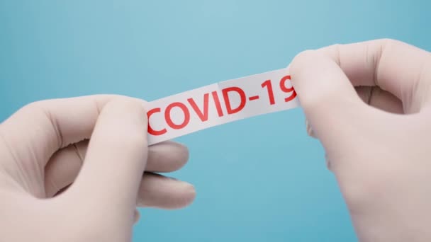 COVID-19を参照。拡散を停止し、コロナウイルスを排除します。伝染病のコロナウイルス。流行の背景。医療の背景。手で青い医療用手袋covid-19プリントで紙を引き裂く — ストック動画