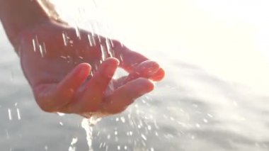 Kadın cupped el deniz manzarası arka plan üzerinde düşen su damlaları yakalar. Güneş kadın elinde parlarken, avuç içine düşen su damlaları. İçki su damlaları ile oynayan kadın el