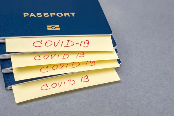 COVID-19 y concepto de viaje. Un trozo de papel con inscripciones covid-19 encerrado en una pila de pasaportes, sobre fondo gris. Epidemia del coronavirus chino. Control de aduanas. Riesgo biológico —  Fotos de Stock