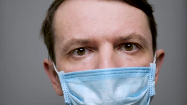 Ongeschoren man doet een beschermend masker af. Beschermende maatregelen. Coronavirus covid-19 sociale afstand. Blanke man kijkt vooruit terwijl hij zijn beschermend masker afdoet — Stockvideo
