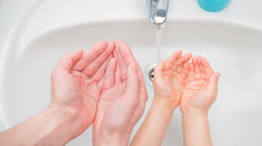 Yıkanan Eller arka planı. Çocuk ve yetişkin elleri lavabonun yanında. Coronavirus COVID-19 hastalığından korunma. El yıkama konsepti. Baba ve oğulun elleri musluktan akan suyla lavabonun üzerinde.