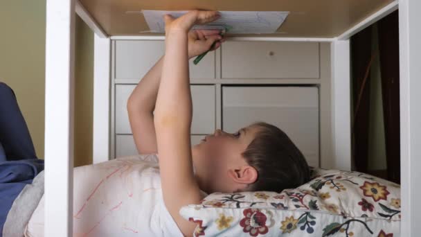 Un garçon peint à l'envers. Loisirs à la maison, intérieur. Dessin d'enfant d'âge préscolaire couché sous la table. Petit peintre dessinant soigneusement sa peinture. Age préscolaire. Apprentissage passionnant. Pensez différemment — Video