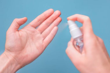 Eller mavi arka plandaki virüslere karşı elleri temizlemek ve korumak için dezenfektan sıkar. Akıllı telefonu dezenfekte eden ellere yakın çekim. Dezenfektanla el temizleme. Salgın arka planı