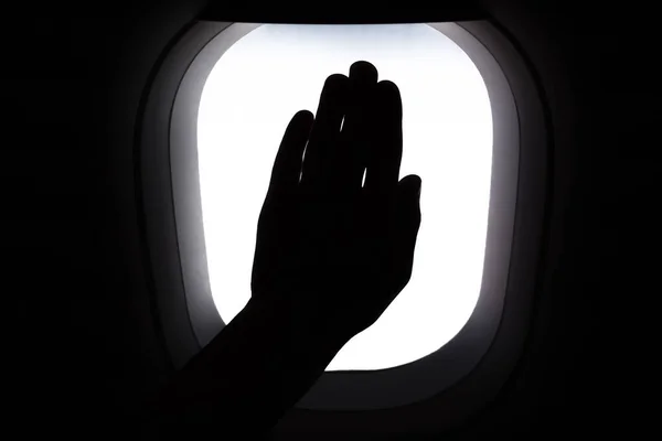 Travel by airplane. Hand on window airplane. Silhouette of hand on window during flight. Missing travel due to COVID-19 pandemic. Memoirs of traveling. Passengers hand on window of airplane. Stop sign