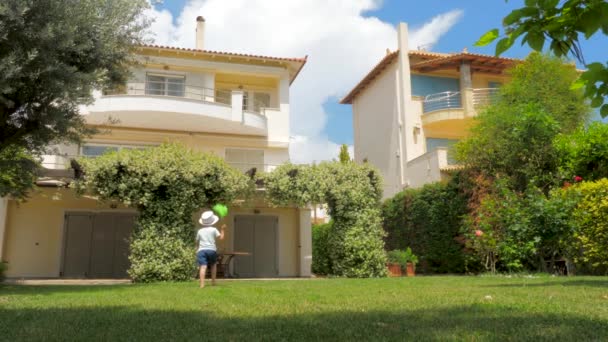 Enfant jouant sur l'herbe verte près de la maison. Un garçon qui court sur une pelouse. Enfant s'amuser avec filet papillon sur herbe verte en face de la maison. Grande maison avec pelouse gazeuse Style de vie familial — Video