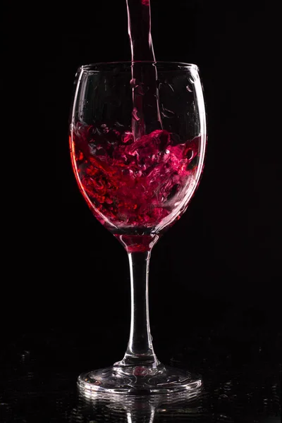 Ein Weinglas auf dunklem Hintergrund ist mit einem roten Getränk gefüllt. — Stockfoto
