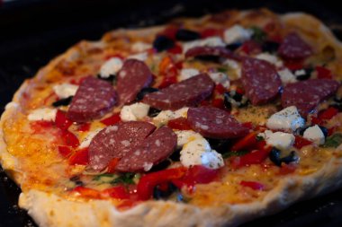 Sıcak, lezzetli, ev yapımı Amerikan pizzası, domatesli salatalık, zeytinli ve kabuklu siyah masa.