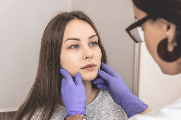 Güzellik uzmanı bir hastanın yüzünü muayene eder. Kozmetik ilaç