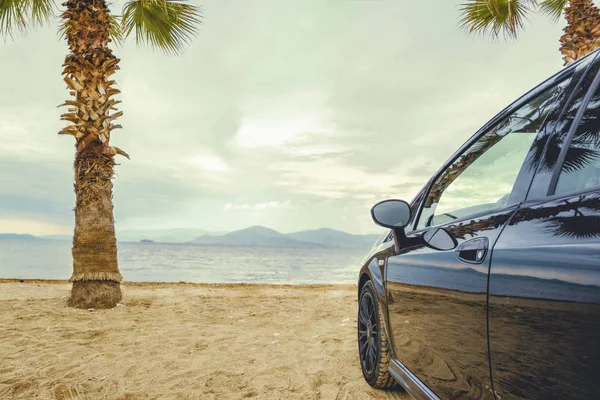 Palmiye ağaçları arasındaki güzel plajda, siyah yaz arabasının yan tarafında. Yaz yolculuğu ve sahilde mola..