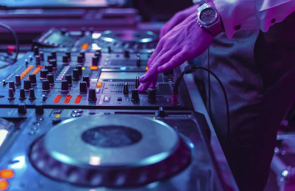 DJ manos mezclando música en la consola del reproductor. Panel de control del mezclador para reproducir música. Tocando un set en vivo en un club nocturno bajo luz de nion. enfoque selectivo — Foto de Stock